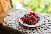 A vibrant display of fresh redcurrant berries arranged on a white plate, set atop an intricate lace tablecloth The natural daylight enhances the rich, red color of the berries, offering a delightful summer vibe