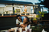 Cheerful African American man hugging girlfriend while resting at table near food truck in evening in park