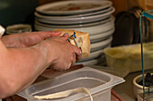 A person expertly slices a large block of cheese, a crucial step in preparing ingredients for making delicious pizzas