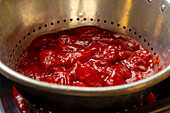 Bright red tomato sauce, rich and chunky, sits in a metallic colander, highlighting the early stages of cooking a homemade pizza