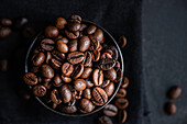 Top view of a dark bowl filled with glossy, fresh coffee beans set against a dark textured background, enhancing the rich textures and deep brown colors.