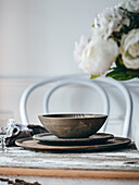 A beautifully arranged rustic table setting featuring wooden plates and a wooden bowl, placed on a weathered wooden table, accentuated by a bouquet of white flowers.