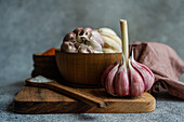 Fresh garlic bulbs and individual cloves displayed on a wooden cutting board, accompanied by a wooden bowl, making a visually rich cooking theme