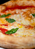 A close-up image showcasing a hot, freshly made pizza adorned with melting cheese, bright red tomato sauce, and fresh green basil leaves, presenting an appealing and delectable appearance