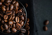 Top view of a dark bowl filled with glossy, fresh coffee beans set against a dark textured background, enhancing the rich textures and deep brown colors.