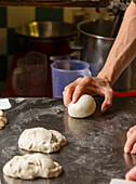 A close-up image capturing the hands of a chef kneading pizza dough on a metallic counter, showcasing the early stages of pizza preparation