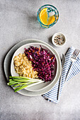 Teller mit gesundem Essen, auf dem fluffig gekochter Bulgur mit einem farbenfrohen Salat aus rohem Rotkohl und Karotten, ergänzt durch frische grüne Zwiebeln und einen orangefarbenen Wasserbecher, angerichtet ist