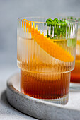 A vibrant summer cocktail featuring cherry liqueur and tonic, served with ice, a fresh orange slice, and mint leaves in a stylish glass on a concrete tray