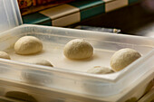 Raw, perfectly shaped pizza dough balls left to rise in a clear, plastic tray, capturing the initial steps of pizza preparation