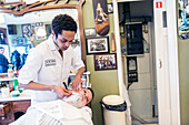 Professioneller Friseur und Haarschneider bei der Rasur seines Kunden im Schorem Barber Shop am Nieuwe Binnenweg, Rotterdam, Niederlande.