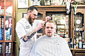 Professioneel barbier verzorgt het haar van een van zijn mannelijke klanten in de barbershop.