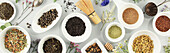 Assortment of dry tea in white ceramic bowls. Matcha, rooibos, black tea, green tea, herbal blend, masala and chamomile tea. Top view, laid flat, banner