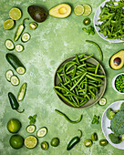 Green vegetables on a green background, including peas, avocado, cucumber, beans, broccoli, tomatoes and peppers