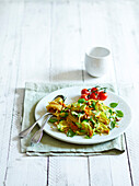 Fried zucchini flowers, fried cherry tomatoes, basil and chopped hazelnuts served with spaghetti on a white wooden background