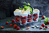 Six strawberry-filled glasses with meringue topping on grey metal background