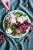 Waldorf-Salat mit Birnen, Walnüssen, Sellerie, Weintrauben und Rucola-Blättern. Weibliche Hand gibt Dressing hinzu.