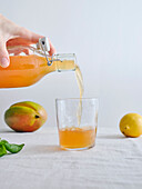 Weibliche Hand gießt hausgemachte fermentierte Bio-Kombucha-Limonade aus einer Flasche in ein Glas