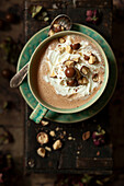 A cup of hot chocolate with a malt flavour in a rustic setting. Topped with cream and crushed malt chocolate balls.