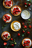 Homemade round strawberry tarts filled with cream, fresh strawberries and strawberry syrup on a grey metal background