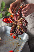 Woman holds raw octopus and smears it with spices and tomatoes.