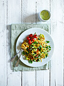 Fried zucchini flowers, fried cherry tomatoes, basil and chopped hazelnuts served with spaghetti on a white wooden background