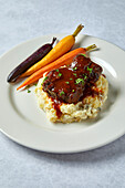 Beef Short Ribs mit Kartoffelpüree und Regenbogenkarotten auf neutralem Hintergrund mit weichen Schatten