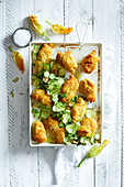 Baked courgette flowers on a white baking tray, served with mini courgette slices on a white wooden background