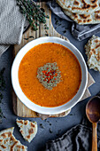 Turkish tarhana soup in a white bowl, garnished with dried mint and red pepper flakes, Turkish bazlama bread, thyme and a wooden spoon accompany.