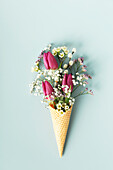 Ice cream cone with beautiful flowers on blue background flat lay top view. Summer minimal concept