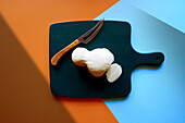 Mozzarella cheese on chopping board, with color blocking and geometric shadow aesthetic.