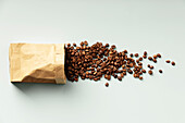 Coffee beans flowing out of a paper bag onto a flat background.