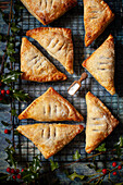 Fruit turnovers made with puff pastry on a wire rack surrounded by holly.