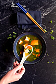 Okinawa style rustic miso soup, closeup with female hand.