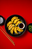 Dumplings in a black bowl with chopsticks on a red background