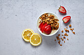 Bowl of lemon and strawberry smoothie with granola on a neutral background with soft shades