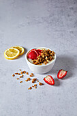 Lemon and strawberry smoothie bowl with granola on a neutral background with soft shadows