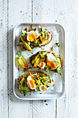 Fried zucchini flowers on baguette slices, served with poached egg and chives on a white wooden background