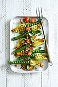 Grilled courgette flowers with cherry tomatoes, basil, chopped hazelnuts and thyme flowers on a white wooden background.