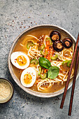 Ramen with noodles, eggs, mushrooms, carrots and sesame seeds on a light background