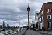 View of the Neuer Zollhof (The New Zollhof), named after a former customs facility, a prominent landmark of Dusseldorf-Hafen, part of the redeveloped port of Dusseldorf,  with the Rheinturm (Rhine Tower) telecommunications tower in the background, Dusseldorf, North Rhine Westphalia, Germany, Europe