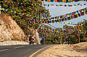 Nepalese prayer flags above a highway with a motorcycle driving by, Kathmandu Valley, Nepal, Asia