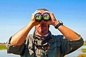 Safari guide watching an elephant (Loxodonta africana) with binoculars, Okawango delta, Botswana, Africa