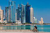 Ein Radfahrer vor der Skyline der West Bay, Doha, Katar, Naher Osten