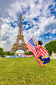 Patriotic American Woman jumping and cheering for Team USA and the Paris 2024 Olympics in front of the Eiffel Tower, Paris, France, Europe