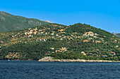 Meerblick auf niedrige Häuser auf dem Hügel und in der Nähe des Strandes, umgeben von grünem Wald, Lefkada, Ionische Insel, Griechische Inseln, Griechenland, Europa