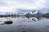 Hohe Berge mit schneebedeckten Gipfeln spiegeln sich im ruhigen Wasser des Fjords bei Flut mit malerischen Wolken, Leknes, Lofoten, Norwegen, Skandinavien, Europa