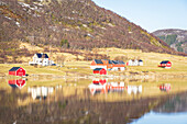 Ländliche Szene mit typischen Gebäuden und Holzhügeln am Fjord, die sich im Wasser spiegeln, Leknes, Lofoten, Norwegen, Skandinavien, Europa