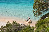 Frau sitzt auf einem Felsen am Strand der Dafines-Bucht, Halbinsel Karaburun, innerhalb des Karaburun-Sazan Marine Parc, Vlore-Bucht, Albanien, Europa