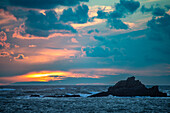 Atemberaubender Sonnenuntergang über der felsigen Küste der Halbinsel Quiberon in der Bretagne, Frankreich. Die leuchtenden Farben des Himmels spiegeln sich in den Wellen des Meeres.