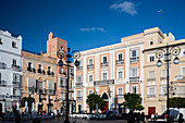 A beautiful sunny day in Cadiz, Andalusia, Spain, showing the vibrant Plaza de San Antonio with historic buildings and outdoor cafes.